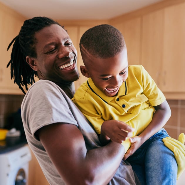 A smiling man lifting a young boy